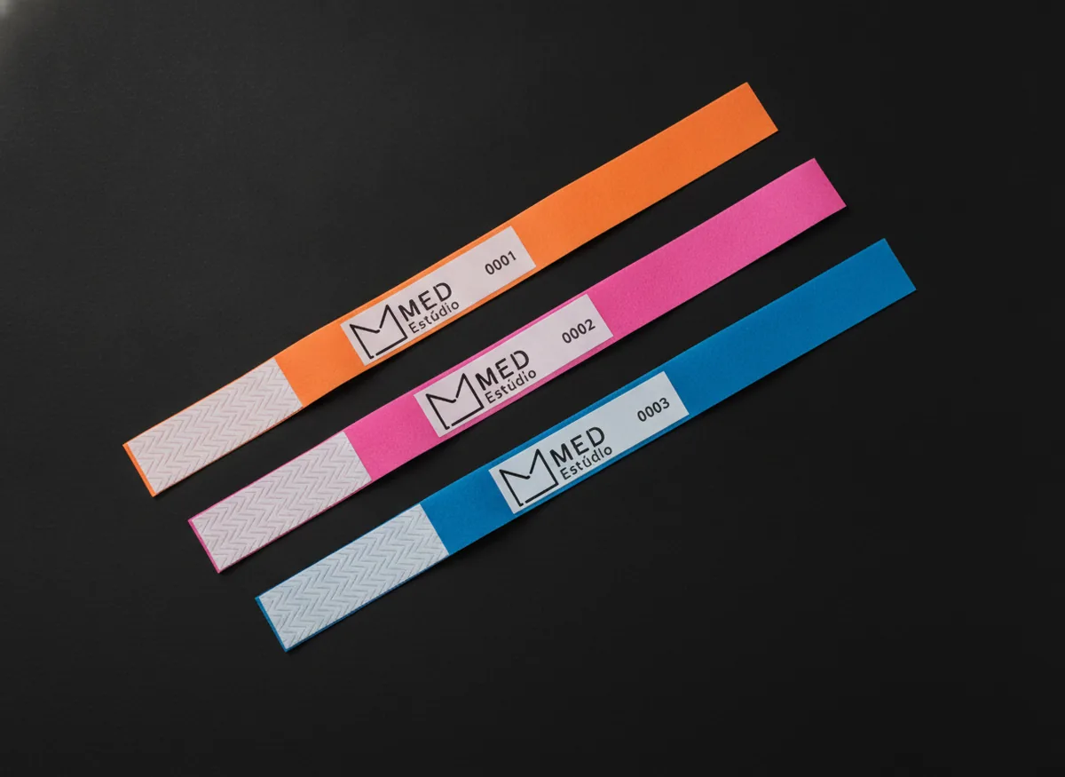 Três pulseiras de Tyvek, laranja, rosa e azul, com o logo da Med Estúdio e numeração sequencial na área branca